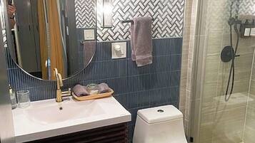Un baño con diseño moderno, que cuenta con un espejo, lavabo, inodoro y ducha.