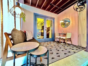 Una habitación con piso estampado, un sofá, dos mesas redondas y una puerta que da a otra estancia.