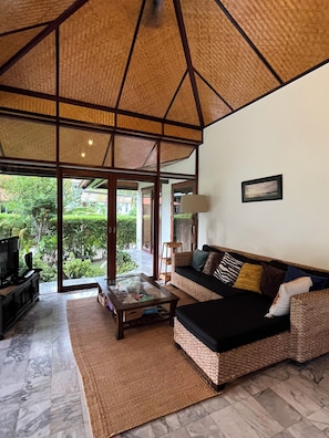 A living room with a sofa, coffee table, and television, a large window with a view of greenery, and a ceiling with a geometric pattern. - Private 3-Bed Villa · Huge 860m² Garden · Mountain View · Gated · Long Stays (Tambon Nong Kae)