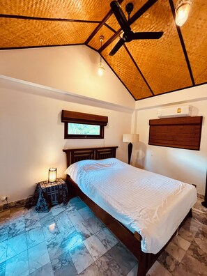Quarto com cama, ventoinha no teto, janela e ar-condicionado fixado na parede.