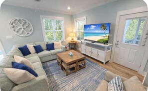 Ein Wohnzimmer mit Sofa, Couchtisch, Fernseher und einer Tür.