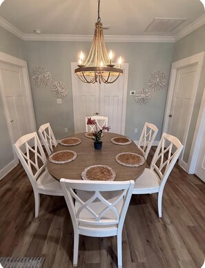 Comedor con una mesa redonda, sillas blancas, una araña y decoración en las paredes.