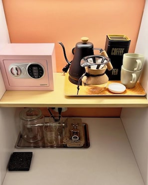 A coffee station with a coffee maker, a grinder, a coffee press, and a mug on a wooden shelf.