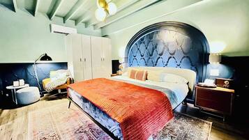 Un dormitorio con una cama grande, cabecera redonda, mesita de noche, lámpara, una silla y una alfombra.