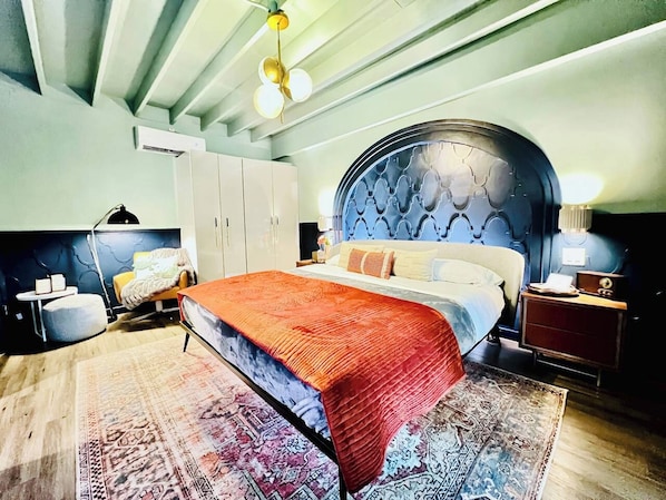 A bedroom with a large bed, a round headboard, a bedside table, a nightstand, a chair, and a rug.