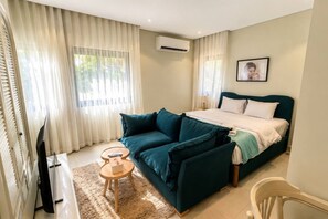 Ein Schlafzimmer mit einem Bett, einem Sofa, einem Fernseher und einem Fenster mit Vorhängen.