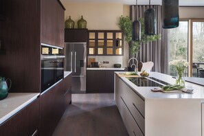 A modern kitchen with dark wood cabinets, stainless steel appliances, and a large island with a sink. - Hyggee House - Stunning Home in a spectacular setting (Calne)