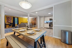 A dining area with a wooden table set for four, a bench, and a modern kitchen in the background. - Spacious 4-bedroom house in charming Durham with private pool and game room (Durham)