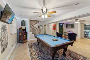 A pool table in a room with a ceiling fan, a dartboard, and a pinball machine. - Spacious 4-bedroom house in charming Durham with private pool and game room (Durham)