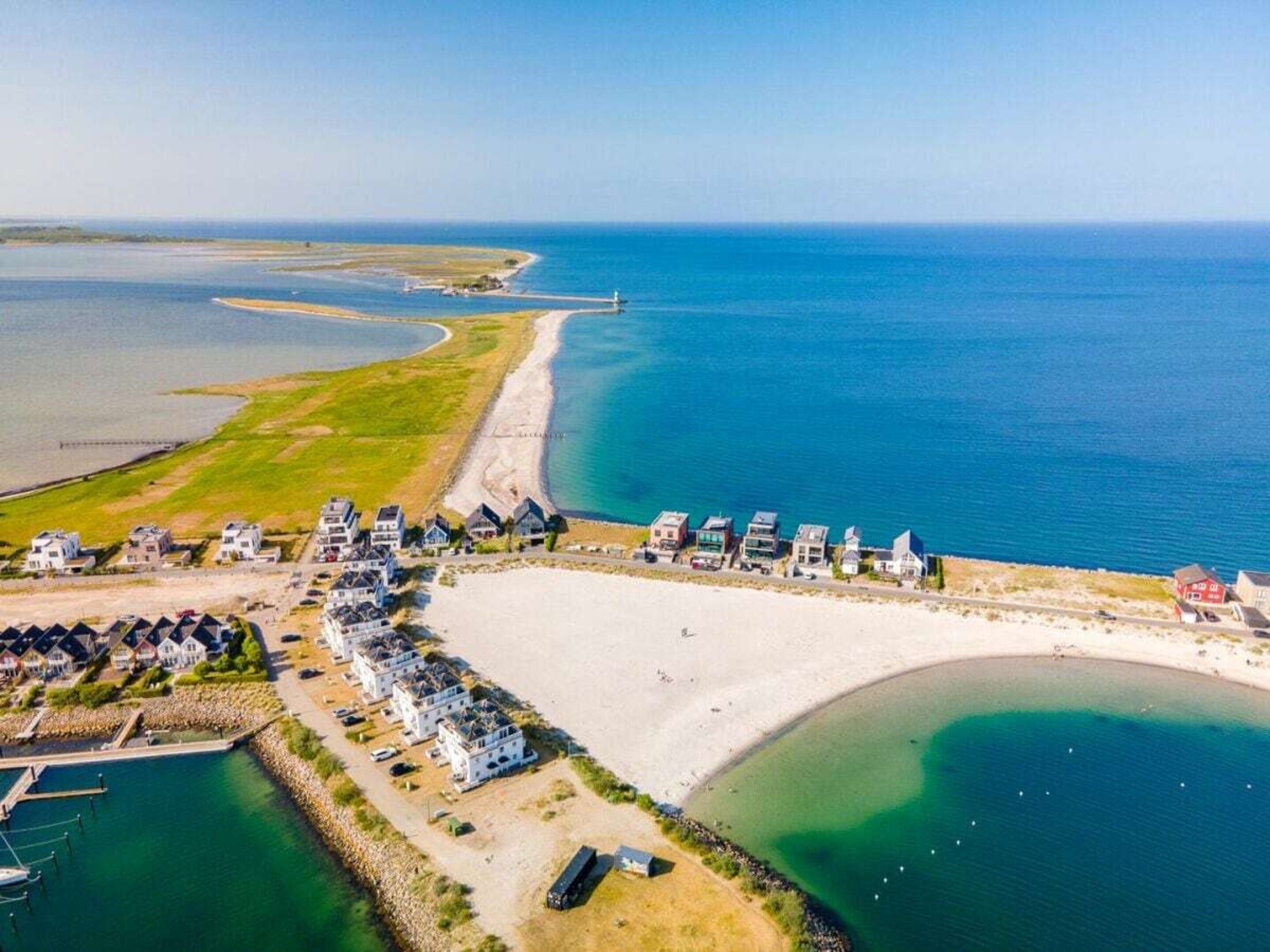 Ovenudblik over en ejendom ved kysten med strand, en lysthavn og en række huse.