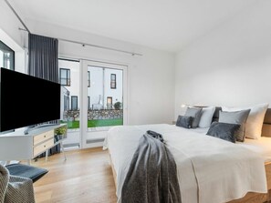 A modern bedroom with a large bed, a flat-screen TV, a desk, and a view of a courtyard through a glass door.