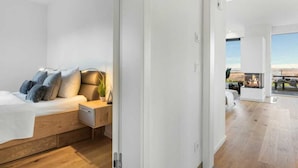 Ein modernes Schlafzimmer mit einem Holzbett, einem Nachttisch und Blick auf einen Balkon mit Kamin.