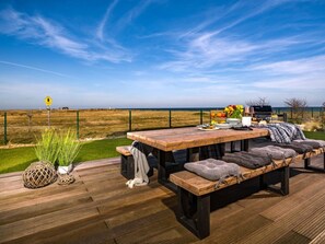 Un espacio de comedor al aire libre con una mesa y bancos de madera, con vistas a un campo cercado y al mar.
