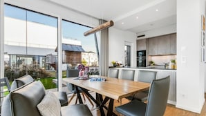 Eine moderne Küche mit dunklen Schränken und einer zentralen Kochinsel, ein Essbereich mit Holztisch und Stühlen sowie eine große Glastür, die in einen Garten führt.