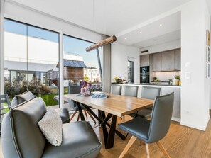 A modern kitchen with dark cabinets and a central island, a dining area with a wooden table and chairs, and a large sliding glass door leading to a garden. - Villa in Kappeln With Swimming Pool (Kappeln)