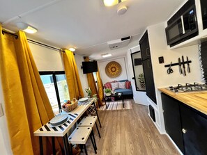 A compact kitchen with a microwave, stove, and a dining area with a table and chairs. - Cozy 1-bedroom mobile home in soothing Miami with AC (Miami)