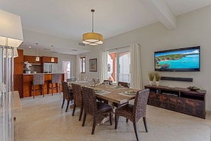 A dining area with a wooden table and chairs, a kitchen in the background, and a TV mounted on the wall. - LUXURY WATERFRONT PENTHOUSE PRIVATE POOL 3 BEDROOM 3 BATHROOM (Lowlands)