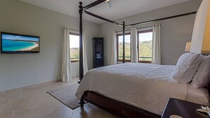 Une chambre à coucher avec un lit à baldaquin, un téléviseur fixé au mur et une vue sur l’extérieur.