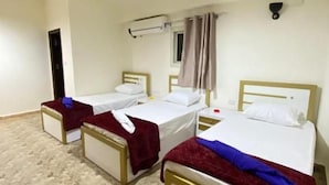 Habitación de hotel con tres camas individuales, una lámpara en el techo, una ventana con cortinas y un equipo de aire acondicionado instalado en la pared.