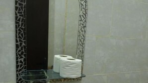 Un baño con lavamanos, espejo y repisa con papel higiénico.