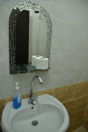 Un bagno con lavandino, specchio e ripiano con carta igienica.
