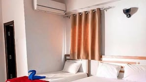 Habitación de hotel con dos camas, una colcha roja y otra blanca, un plaid rojo sobre la cama blanca, cabecero de madera, aire acondicionado de pared y una cortina.