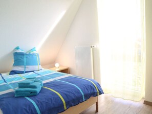A bedroom with a bed, pillows, a nightstand, a lamp, and a window with curtains. - Holiday Home in Wittmund With Swimming Pool (Wittmund)