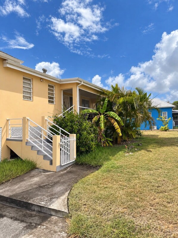 A two-story building with a covered porch, a staircase with a railing, and a well-maintained lawn with palm trees.