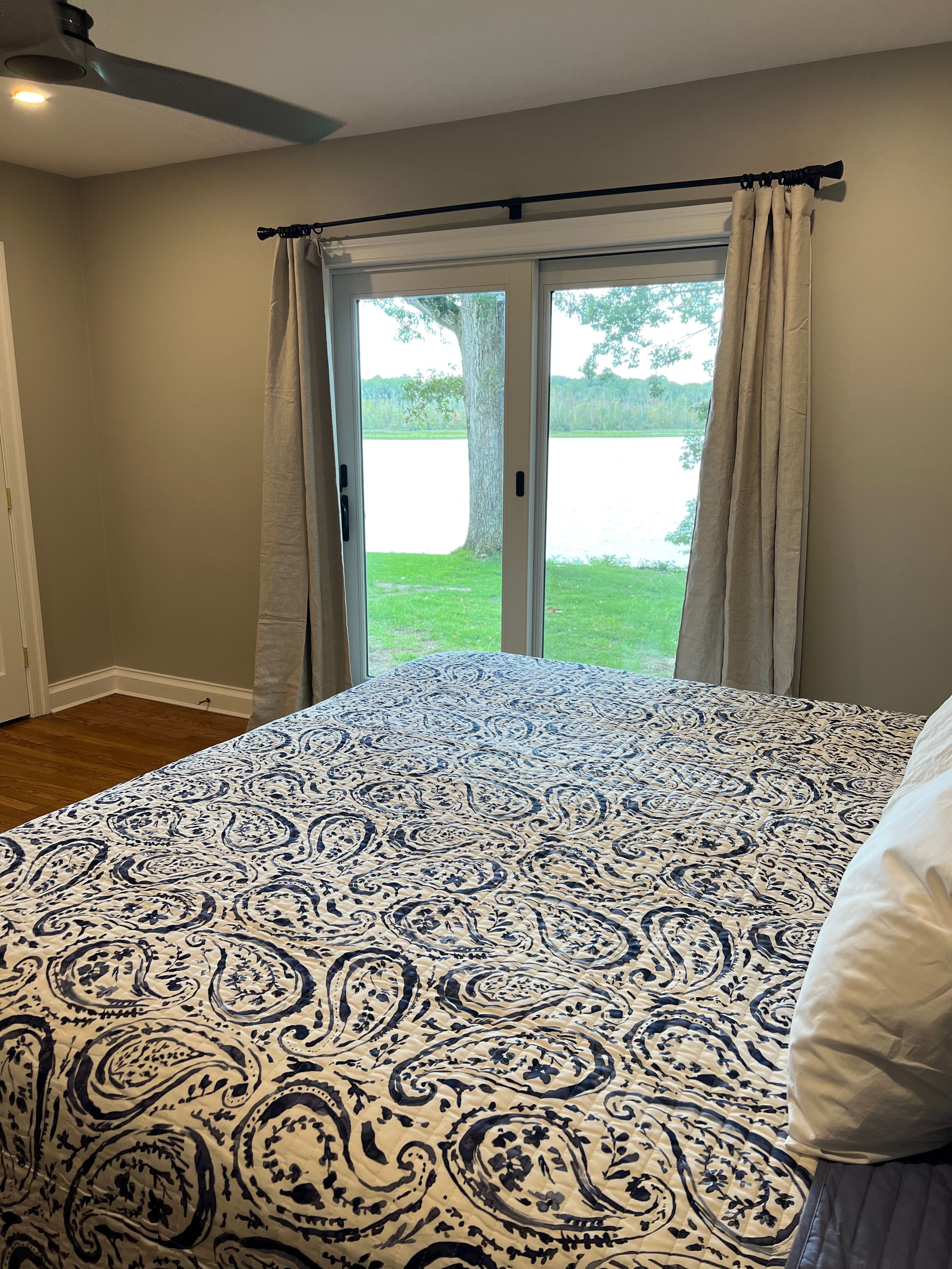 A bedroom with a large bed, a window with curtains, and a view of a lake.