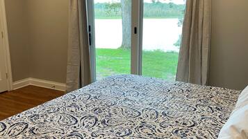 A bedroom with a large bed, a window with curtains, and a view of a lake.