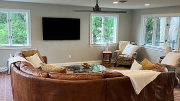 Un salón amplio con un sofá seccional en forma de L, una mesa de centro de vidrio y un televisor de pantalla plana montado en la pared.
