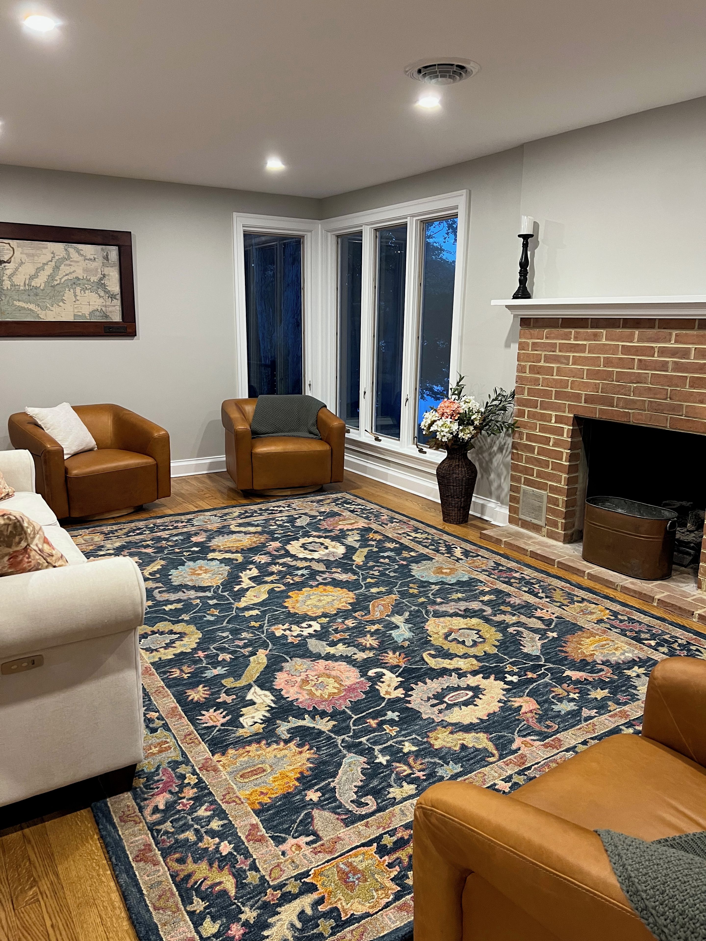 A living room with a large window, a fireplace, and a patterned rug.