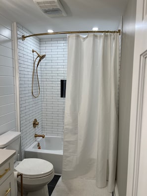 Un bany amb un vàter blanc, una banyera i una dutxa amb cortina.