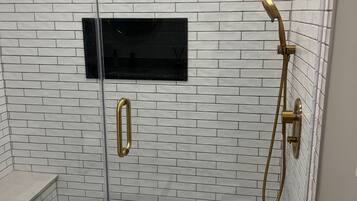A shower with a glass door, a handheld showerhead, and a rectangular black panel on the wall.