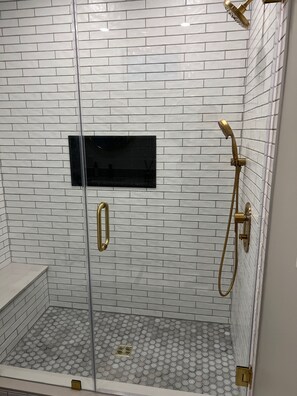Chuveiro com porta de vidro, chuveiro manual e um painel preto retangular na parede.