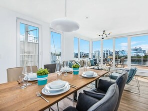 Ein Essbereich mit einem Holztisch, gedeckt für vier Personen, große Fenster mit Blick auf die Stadt und eine moderne Kronleuchter.
