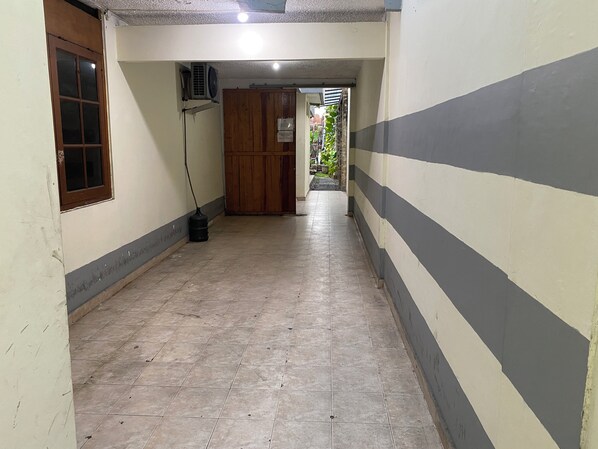 A corridor with tiled flooring, a wooden door, and a wall with a striped pattern.