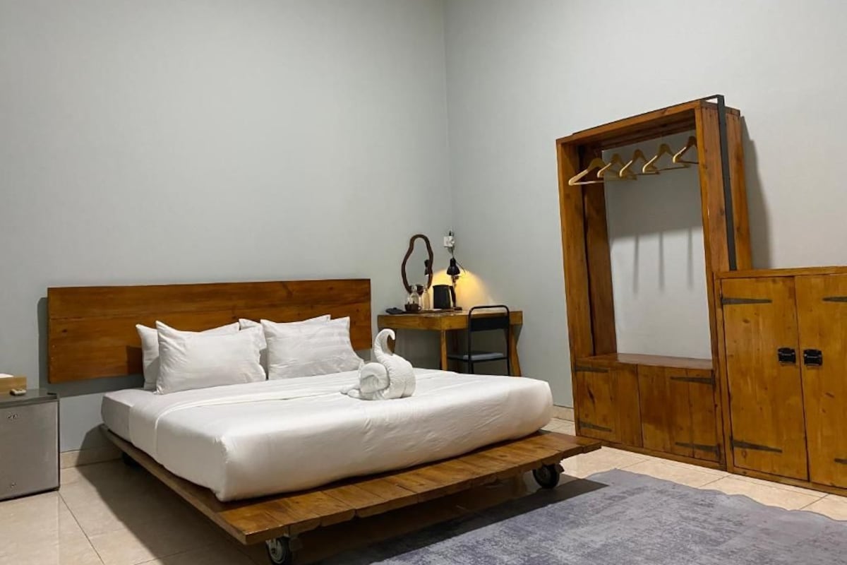 A bedroom with a wooden bed, a desk, a chair, a mirror, and a wardrobe.