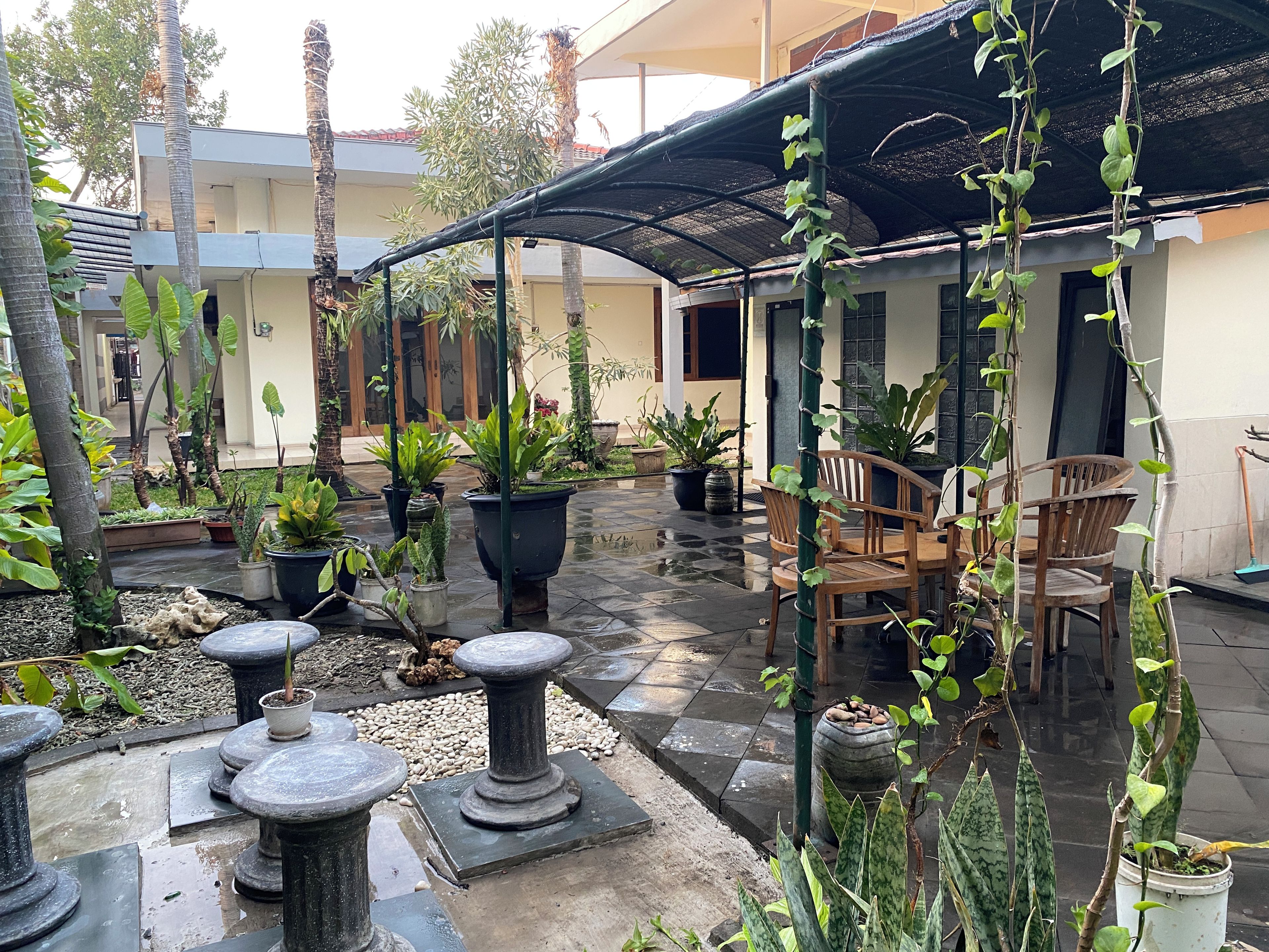 An outdoor patio area with potted plants, stone tables, and wooden chairs.