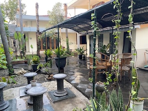 An outdoor patio area with potted plants, stone tables, and wooden chairs.