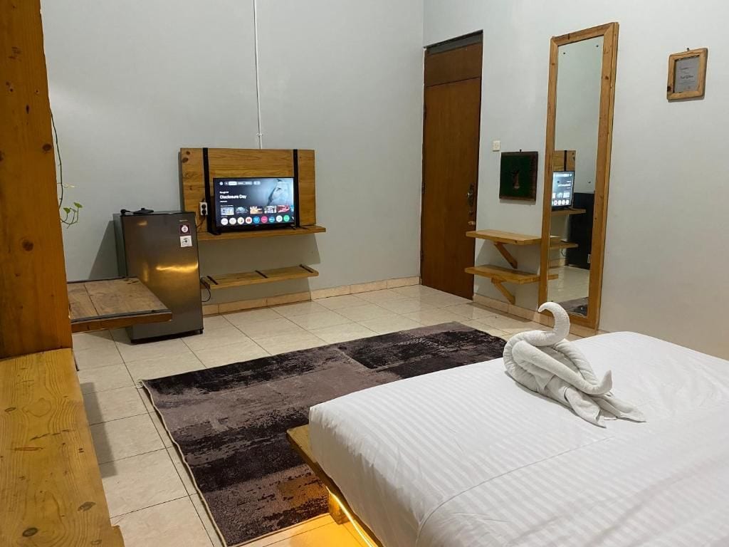 Habitación de hotel con una cama, un televisor sobre un mueble de madera, un refrigerador, un armario de madera y un espejo.