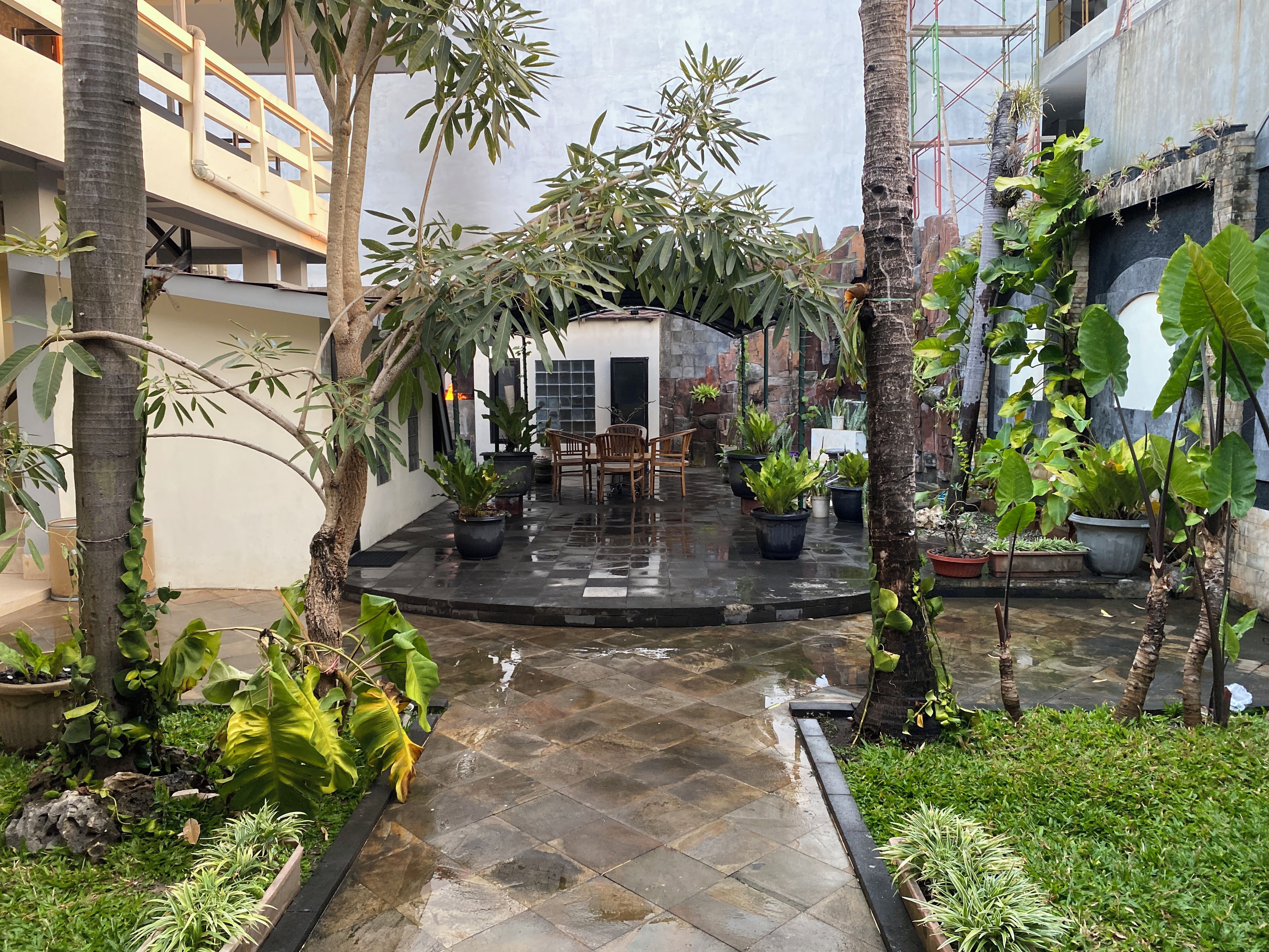 Une cour intérieure avec un espace de repos central, entourée de plantes en pot et d’arbres.