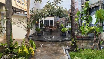 Une cour intérieure avec un espace de repos central, entourée de plantes en pot et d’arbres.