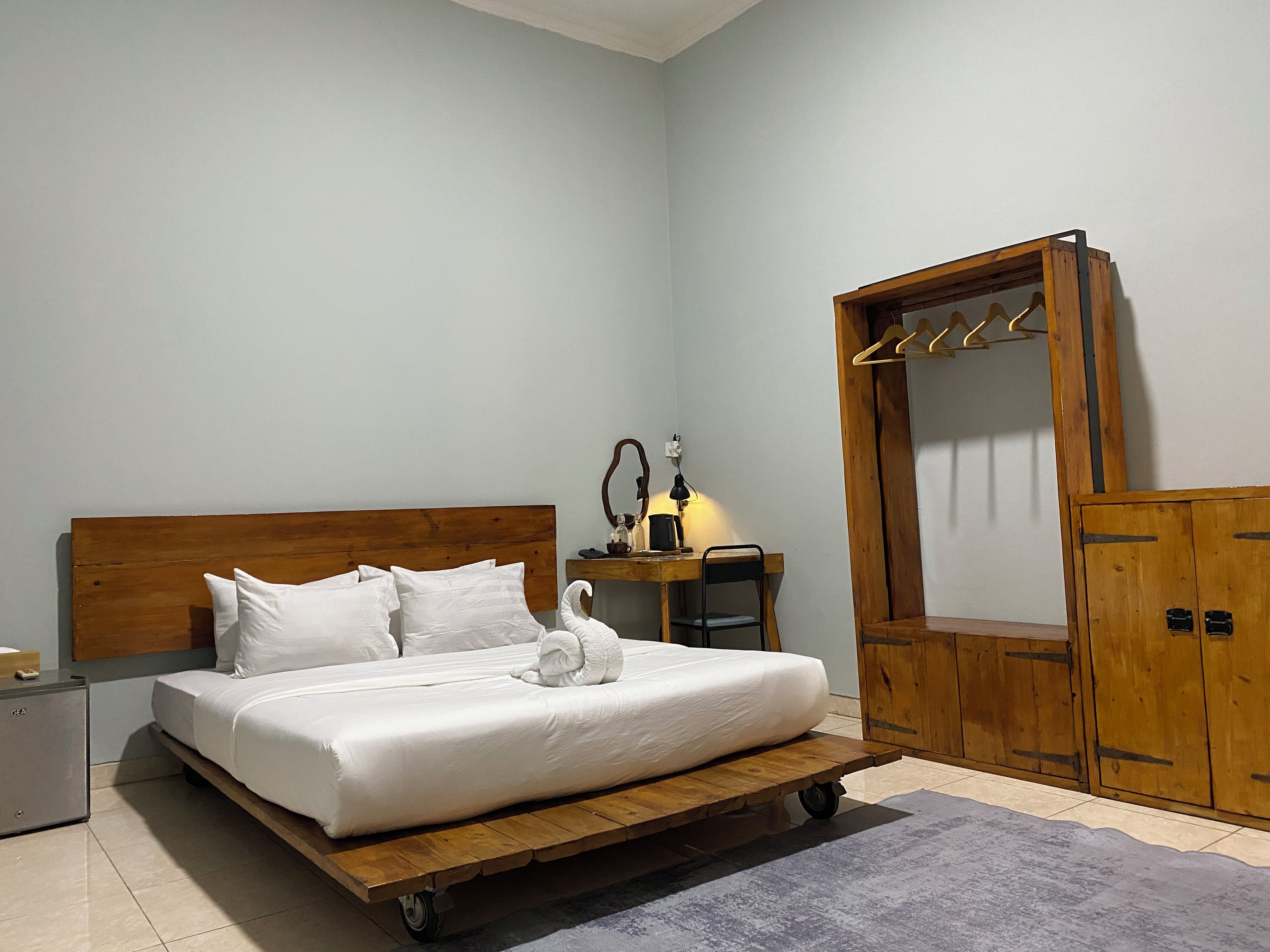 Ein Schlafzimmer mit einem hölzernen Bett, einem kleinen Nachttisch, einem Schreibtisch mit Stuhl, einem Holzschrank und einem Spiegel.