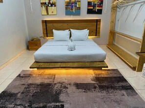 A bedroom with a wooden headboard, a bed with white bedding, a decorative sculpture, and a dark patterned rug.