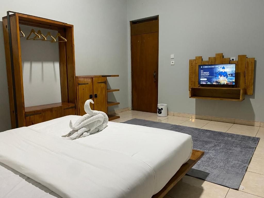Quarto de hotel com cama, guarda-roupa de madeira, televisão na parede e uma porta.