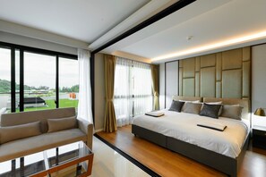 A modern hotel room with a large bed, a sofa, a glass coffee table, and a view of a green landscape. - Surin - Freshly Renovated Stay (Thalang District)