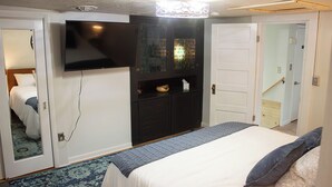 Un dormitorio con cama, televisor, armario y puerta que da a otra habitación.