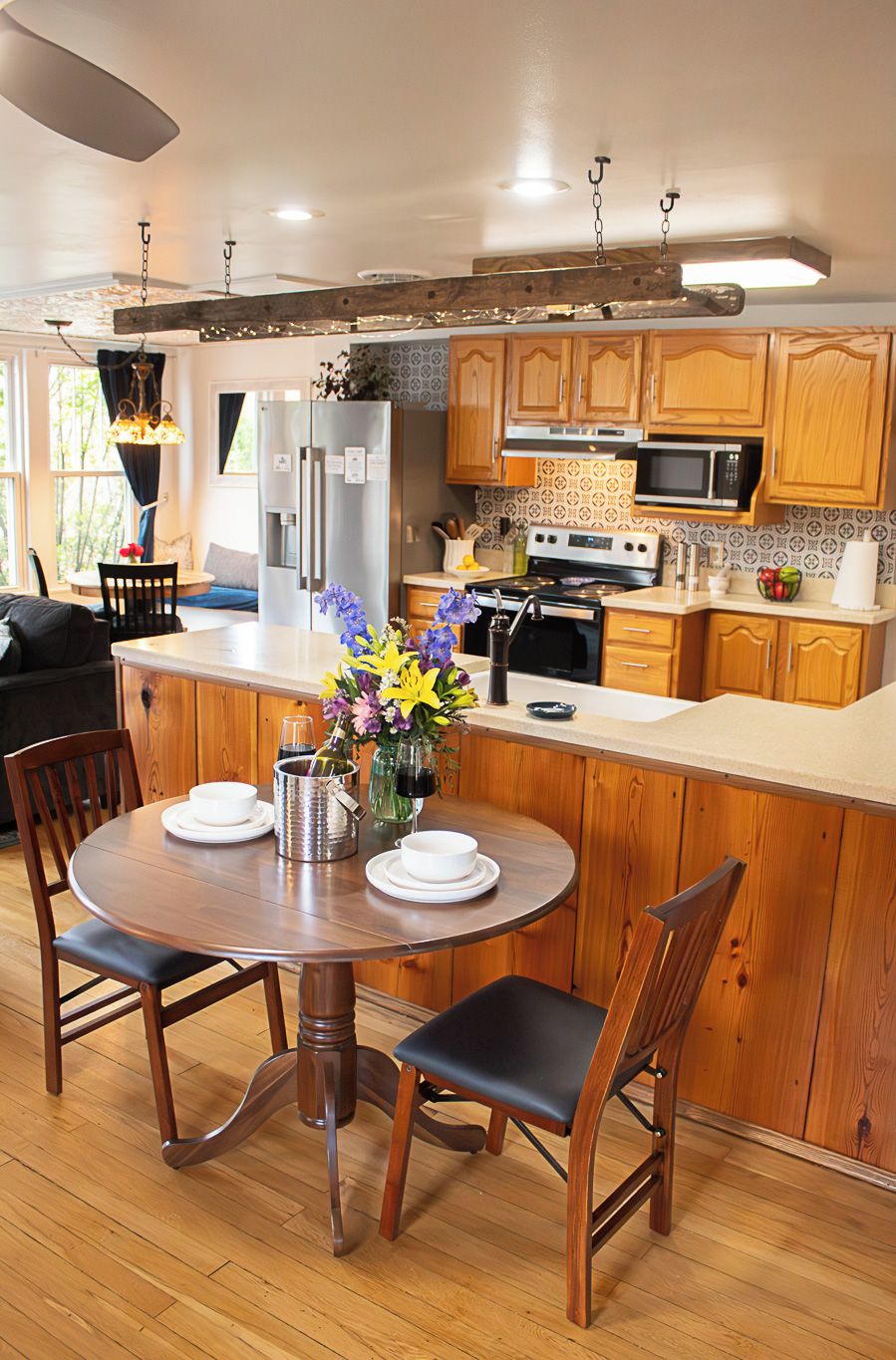 Een moderne keuken met houten kastjes, een centraal eiland en een eethoek met een ronde tafel en stoelen.