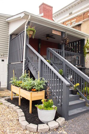 A residential building with a front porch, a wooden staircase, and raised garden beds with plants. - Downing Suite Moorefield W.V. (Moorefield)